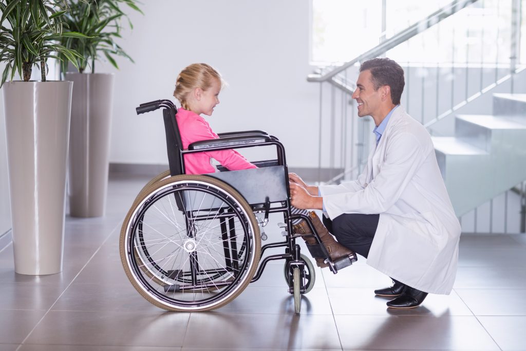Smiling doctor talking to disable girl in hospital corridor