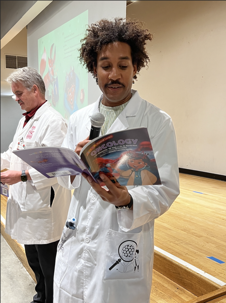 Figure 6: Featured scientist DJ Fernandez & author Dr. W. Martin Kast reading their book aloud to 400 elementary students. Photo by Dieuwertje Kast